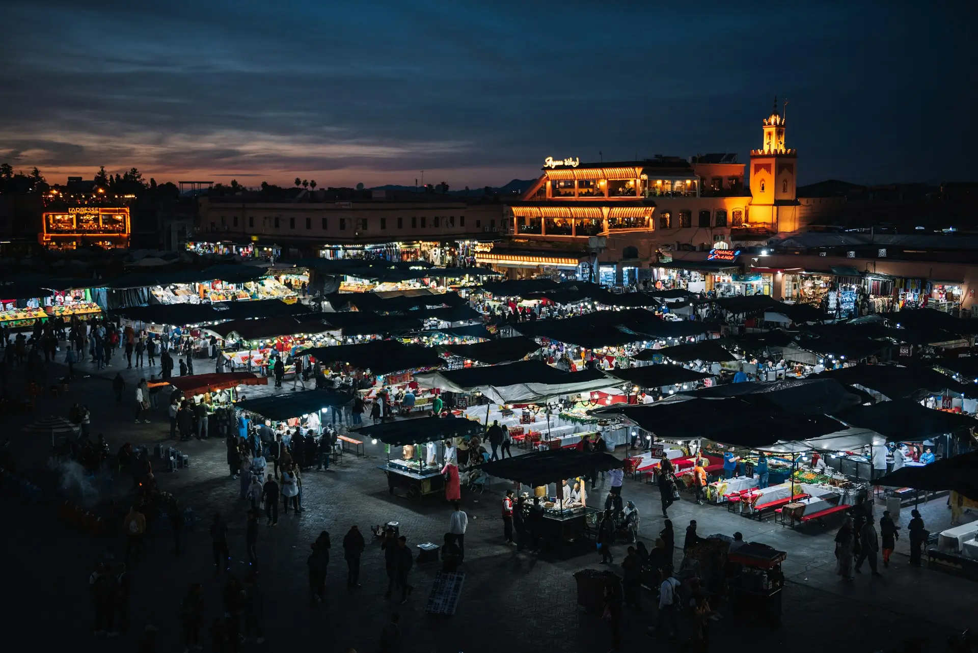 Illuminated Jemaa el-Fnaa night market stalls and Marrakesh skyline at twilight.