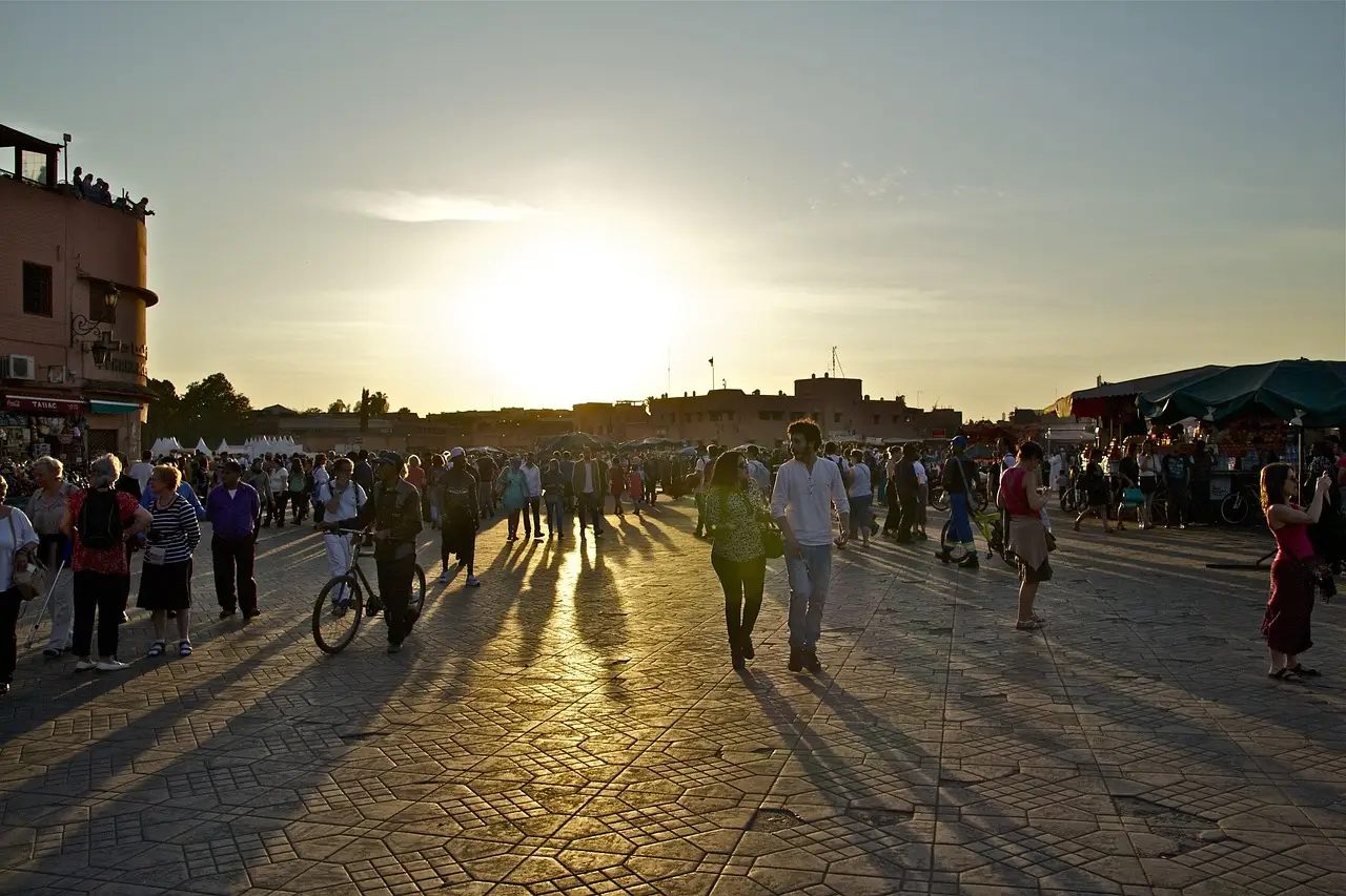 Crowded Jemaa el-Fnaa square in Marrakesh, Morocco, at sunset with long shadows stretching across the stone-paved plaza