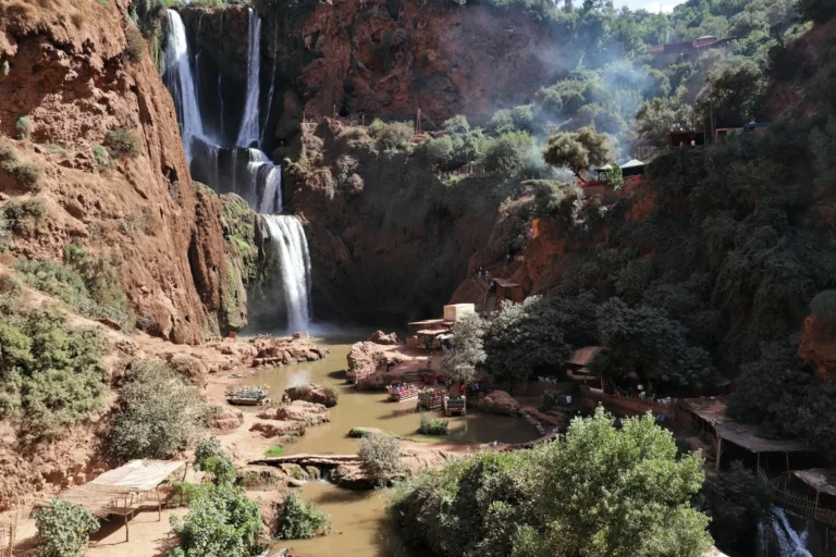 Ouzoud Waterfalls in Morocco surrounded by red cliffs, lush greenery, and traditional riverside cafes