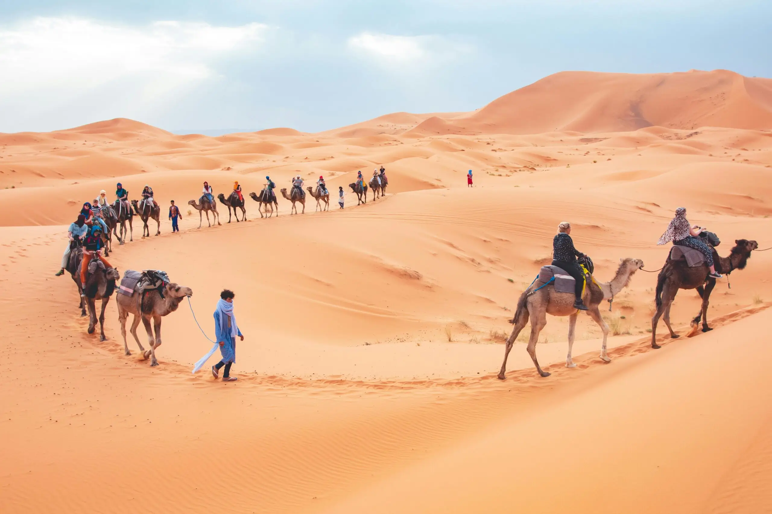 Tourists on a guided camel caravan trekking across golden sand dunes in Merzouga Desert, Morocco, during a 3-day Sahara desert tour from Marrakech.