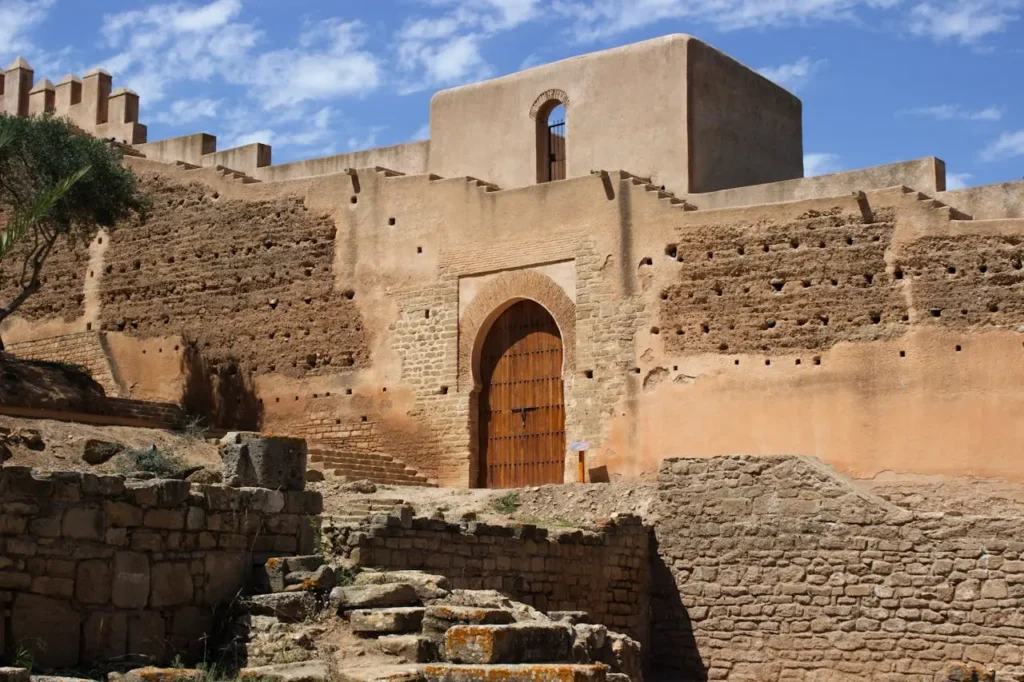 An impressive arched wooden gate set within a thick, ancient stone and mud-brick wall of a Moroccan fortress.