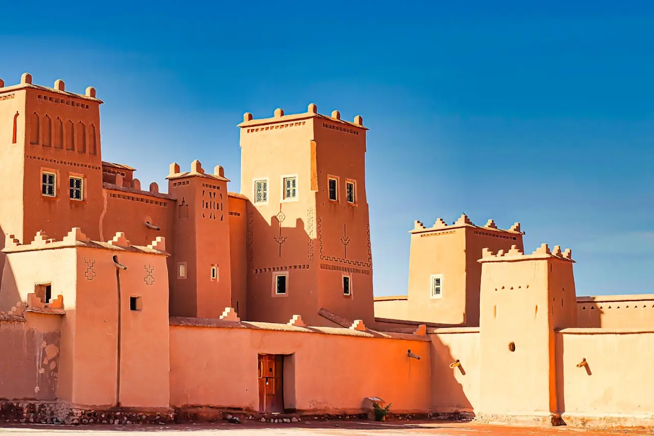 A striking clay Kasbah with a tall, square tower and crenellated battlements against a vibrant blue sky.