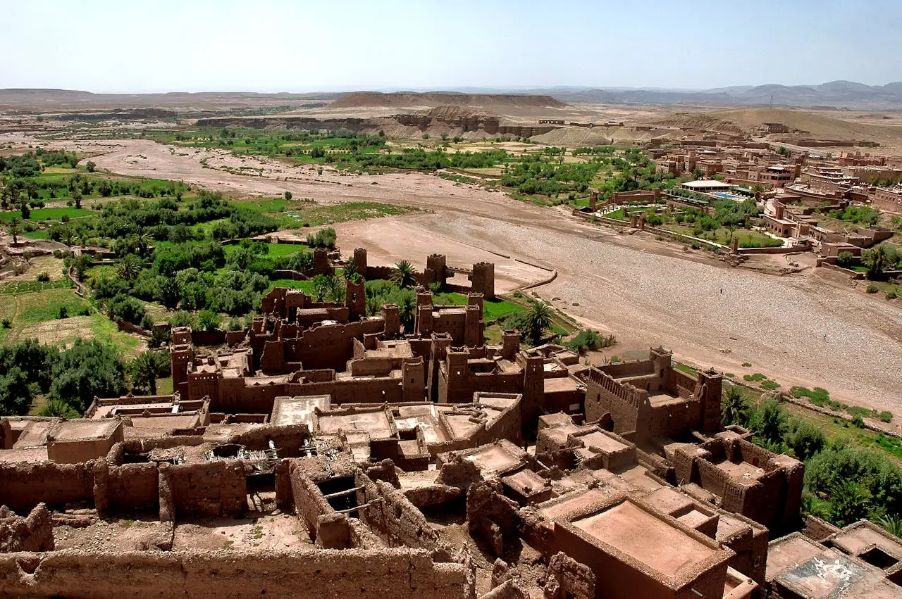 Aerial view of traditional kasbah and green oasis along the river in southern Morocco desert landscape