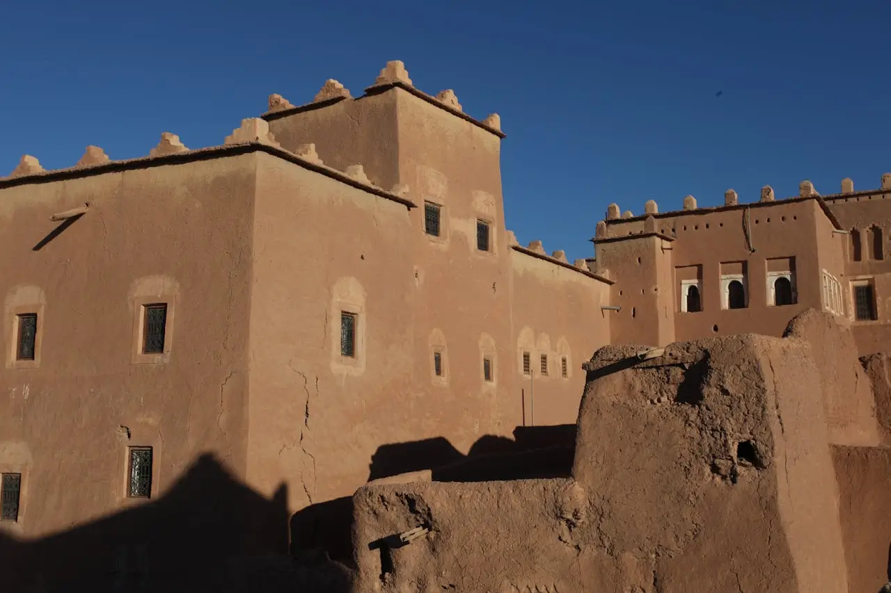 A view of several interconnected clay Kasbah buildings with numerous small windows and decorative crenellated rooftops under a blue sky.