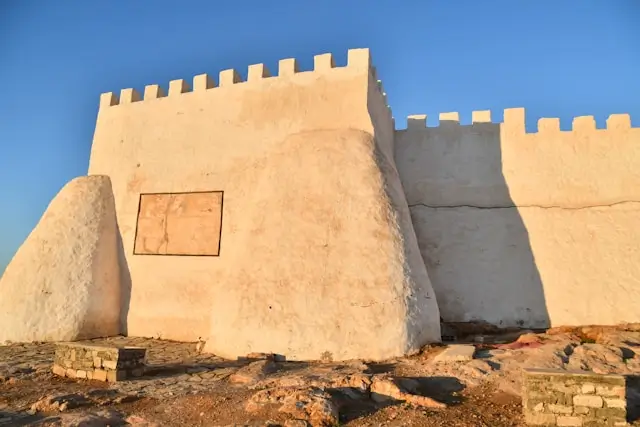 Traditional Moroccan desert kasbah with white fortified walls and crenellations under a clear blue sky.