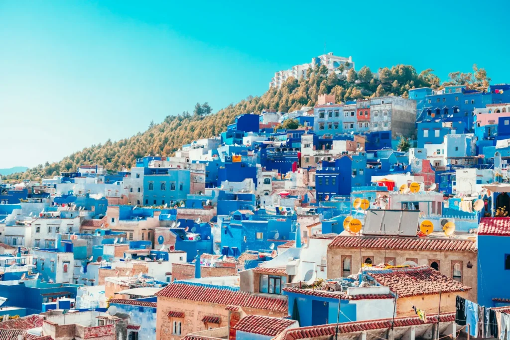 A hillside covered with houses painted in different shades of blue and white, forming the iconic cityscape of Chefchaouen, Morocco.