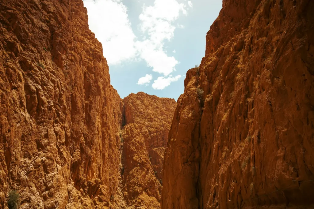 Towering orange rock walls of the Todra Gorge in Morocco, with a narrow strip of blue sky visible above.